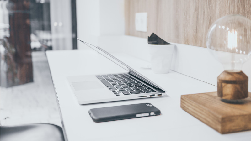 Ein Bürotisch mit Laptop, Handy und Lampe ist zu sehen.